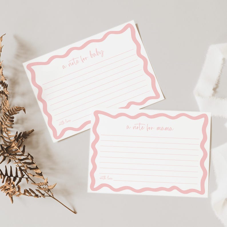 two blank note cards with a pink border, placed on a light-colored surface alongside some dried leaves.