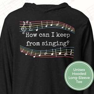 May include: Black hooded long-sleeve tee with musical notes and the text "How can I keep from singing?" The musical notes are in a rainbow of colors. A green circle with white text reads "Unisex Hooded Long-Sleeve Tee."