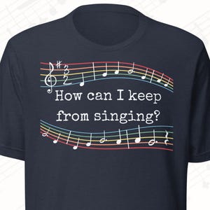 May include: Navy blue t-shirt with musical notes and the text "How can I keep from singing?" The design features a treble clef, musical notes, and colorful staff lines. A fun and musical themed tee.