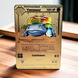 May include: Gold foil Pokemon trading card featuring Venusaur, a Grass-type Pokemon. The card has a gold background with a blue and green illustration of Venusaur. The card text reads "Venusaur 100 HP" and "Seed Pokemon. Length 6'7", Weight: 221 lbs."