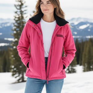 May include: A bright pink winter jacket with a black collar and black accents. The jacket has a zipper and snap closures, and pockets. The person is wearing a white t-shirt and blue jeans. The background shows a snowy mountain landscape.
