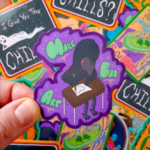 May include: A purple sticker with a cartoon gorilla drawing a heart on a desk. The sticker reads "Make Bad Art" in green and white bubble letters. Other stickers with text and illustrations are in the background.