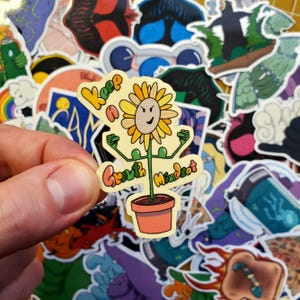 Puede incluir: Una pegatina amarilla y verde con un girasol de dibujos animados en una maceta. La pegatina dice "Keep a Growth Mindset".