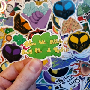 以下が含まれることがあります： 黄色とオレンジの文字で「Those Who Pollute Smell Like A Toot!」と書かれた緑色のステッカー。ステッカーは他のカラフルなステッカーに囲まれている。