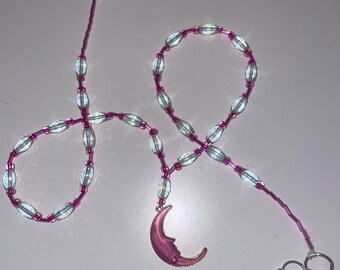 May include: A pink and white beaded necklace with a crescent moon charm. The necklace has a silver T-bar clasp and three silver jump rings.