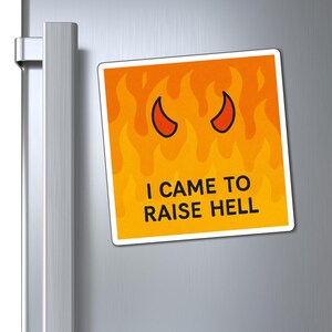 May include: A square magnet with a fiery orange background and black devil horns. The text "I CAME TO RAISE HELL" is printed in white. The magnet is attached to a silver refrigerator door.