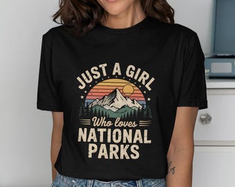 May include: Black t-shirt with a vintage-style graphic that says "Just a girl who loves National Parks". The graphic features a mountain range with a sunset behind it.