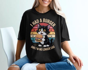May include: Black t-shirt with a graphic of a black and white cat holding a burger. The text on the shirt reads "I had a burger and I'm no longer sad" in a retro style.