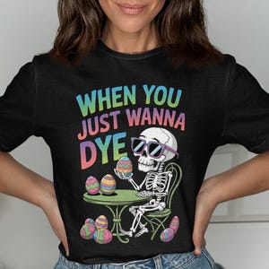 Puede incluir: Camiseta negra con un esqueleto que lleva gafas de sol y sostiene un huevo de Pascua. El texto "When you just wanna dye" está impreso en la camiseta en colores arcoíris.