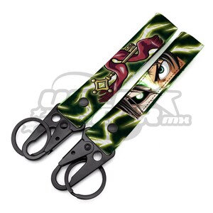 Puede incluir: Llavero negro y verde con un ojo verde y una llave roja con un diseño dorado. El llavero tiene un clip de metal negro.