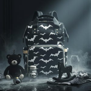 Puede incluir: Un bolso cambiador negro y blanco con estampado de murciélagos y accesorios a juego, como un osito de peluche, un chupete y un caballito balancín. También hay un pequeño tarro con una calavera y un objeto con forma de ataúd. Los artículos están sobre una mesa redonda oscura.