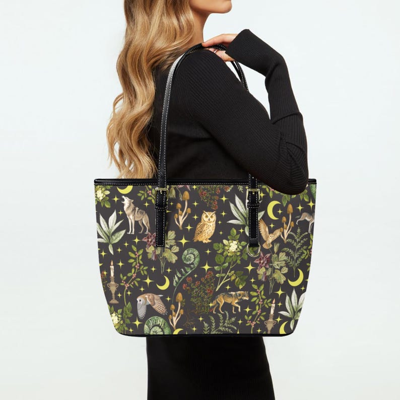 May include: Black tote bag with a whimsical forest pattern featuring wolves, owls, mushrooms, and crescent moons. The bag has black handles and trim, with gold-colored hardware.