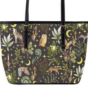 May include: A black tote bag with a repeating pattern of wolves, owls, mushrooms, plants, moons, and stars. The bag has black handles and trim. The design features shades of green, yellow, and brown.