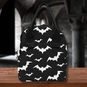 Könnte beinhalten: Schwarze Lunchtasche mit einem weißen Fledermausmuster.