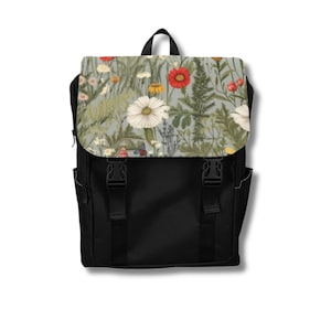 May include: Black backpack with a flap featuring a floral design. The flap showcases a pattern of white daisies, red poppies, and other wildflowers against a light blue background. The backpack has two side pockets and adjustable straps.
