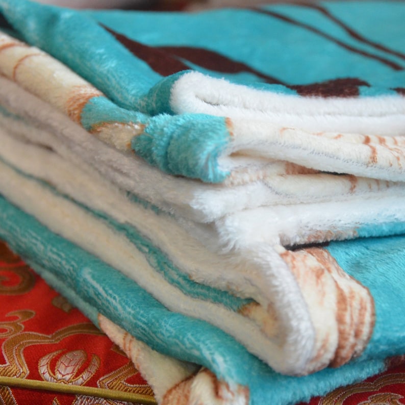 Pu&ograve; includere: Una pila di coperte morbide e soffici. Le coperte presentano un motivo di verde acqua, bianco e marrone. I bordi delle coperte sono verde acqua. Le coperte sono piegate con cura, mostrando i diversi strati e motivi.
