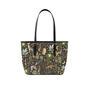 May include: Black tote bag with a whimsical forest pattern featuring wolves, owls, and botanical elements. The bag has black handles and trim, and a black interior. The design includes yellow moons and stars.