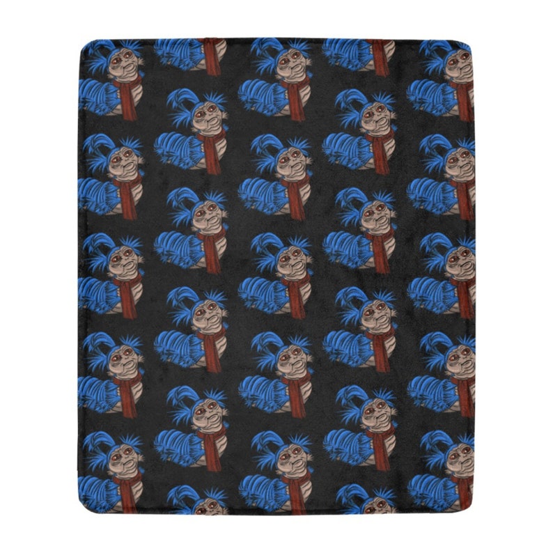 Pu&ograve; includere: Una coperta in peluche con un motivo ripetuto di una creatura blu a forma di verme con una sciarpa rossa. La creatura ha un viso marrone chiaro e capelli blu. Lo sfondo &egrave; nero.