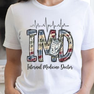 Puede incluir: Camiseta blanca con las letras "IMD" en un diseño médico, con un estetoscopio y una línea de latidos. El texto "Internal Medicine Doctor" está impreso debajo. La persona lleva pantalones cortos vaqueros.