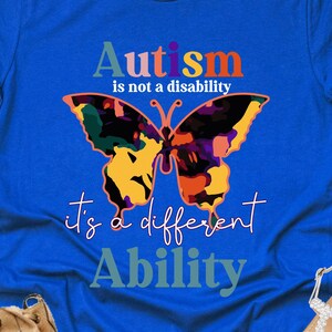 May include: Royal blue t-shirt with the text "Autism is not a disability, it's a different Ability" and a colorful butterfly graphic. The shirt is part of a casual wear collection.