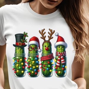 K&ouml;nnte beinhalten: Wei&szlig;es T-Shirt mit einem festlichen Design von vier Cartoon-Gurken in Gl&auml;sern. Jede Gurke ist f&uuml;r Weihnachten mit H&uuml;ten, Geweihen und Schals gekleidet und mit bunten Lichterketten geschm&uuml;ckt.