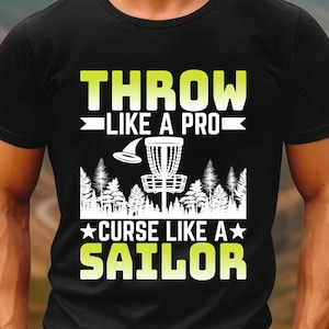 May include: Black t-shirt with a green and white graphic. The text reads "THROW LIKE A PRO" above an image of a disc golf basket and a flying disc. Below the basket, the text reads "CURSE LIKE A SAILOR".
