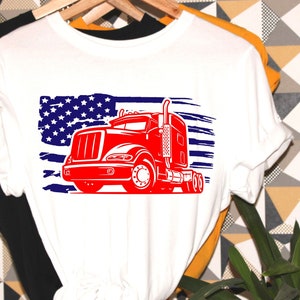 May include: White t-shirt with a red semi-truck graphic in front of an American flag design.