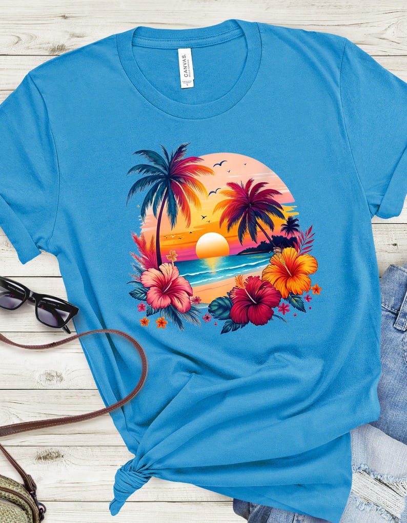 May include: A bright blue t-shirt with a colorful sunset scene featuring palm trees, flowers, and a beach. The design is centered on the shirt.
