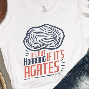 May include: White t-shirt with a blue and white agate graphic and the text "It's not hoarding if it's agates".