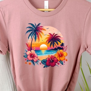 May include: A pink t-shirt with a graphic print of a tropical sunset scene with palm trees, a beach, and hibiscus flowers.