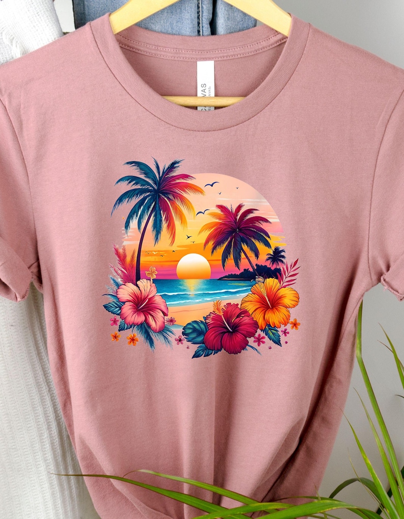 May include: A pink t-shirt with a graphic print of a tropical sunset scene with palm trees, a beach, and hibiscus flowers.
