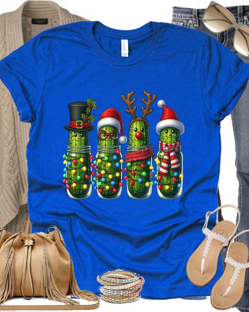 K&ouml;nnte beinhalten: K&ouml;nigsblaues T-Shirt mit einem weihnachtlichen Design. Das Design zeigt vier anthropomorphe Gurken in Gl&auml;sern, die jeweils mit festlichen Accessoires wie H&uuml;ten und Rentiergeweihen geschm&uuml;ckt sind. Die Gurken sind mit bunten Weihnachtslichtern verziert.