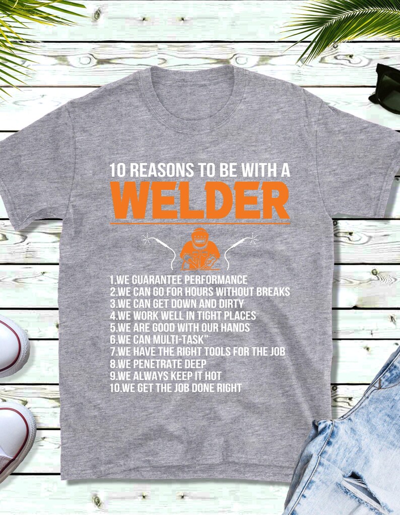 May include: A grey t-shirt with the text "10 REASONS TO BE WITH A WELDER" in orange and white. Below the text is a graphic of a welder. The shirt lists ten reasons to be with a welder.