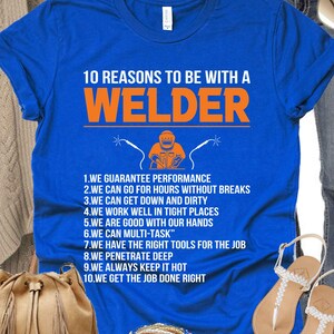 May include: A royal blue t-shirt with the text "10 REASONS TO BE WITH A WELDER" in orange. The shirt features a graphic of a welder and a list of reasons. The shirt is displayed with accessories.