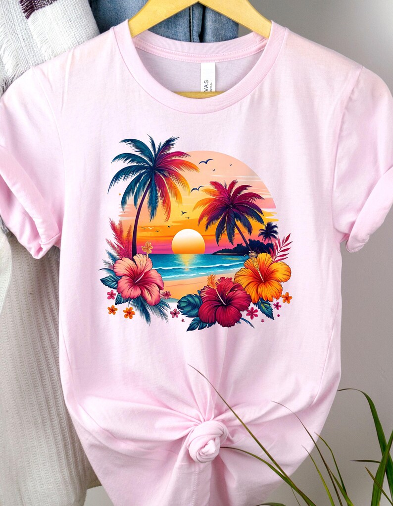 May include: Pink t-shirt with a graphic of a tropical sunset scene with palm trees, a beach, and hibiscus flowers.
