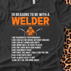 May include: Black t-shirt with the text "10 REASONS TO BE WITH A WELDER" in orange. The shirt features a graphic of a welder and welding tools. The reasons are listed below the graphic.