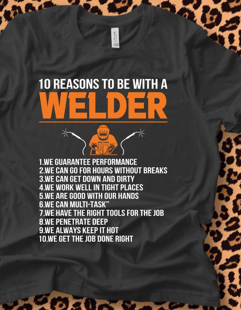 May include: Black t-shirt with the text "10 REASONS TO BE WITH A WELDER" in orange. The shirt features a graphic of a welder and welding tools. The reasons are listed below the graphic.