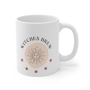Peut inclure: Une tasse en céramique blanche avec une illustration en noir et blanc d'un soleil avec un visage et le texte "Witches Brew" en cercle autour de lui. Cinq petites étoiles rouges entourent le soleil.