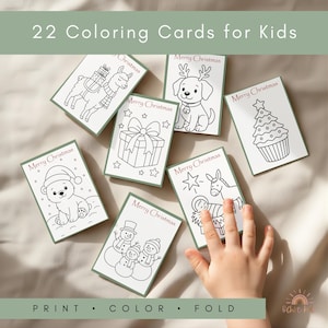 May include: A set of 22 coloring cards for kids, featuring Christmas-themed illustrations. Each card has a white background with a green border and includes images of a llama, dog, gift, bear, snowman, star, donkey, and Christmas tree. The text "Merry Christmas" is printed on each card.