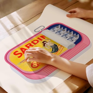 May include: A pink and yellow sardine can illustration with the word "SARDIN" in large red letters. The can features a mermaid graphic and a row of fish. The illustration is on a white surface.
