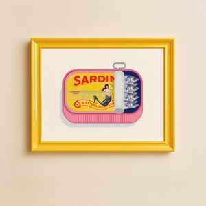 May include: A framed print featuring a pink sardine can with the word "SARDIN" in bold letters. The can's label depicts a mermaid and the text "IN EXTRA VIRGIN OLIVE OIL". The can contains several sardines.