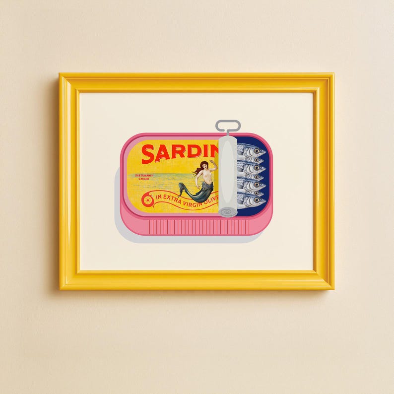 May include: A framed print featuring a pink sardine can with the word "SARDIN" in bold letters. The can's label depicts a mermaid and the text "IN EXTRA VIRGIN OLIVE OIL". The can contains several sardines.
