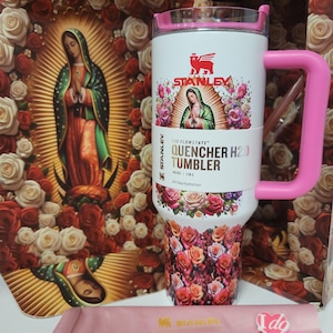 May include: A white 40 oz Stanley Flowstate Quencher H2.0 tumbler with a pink handle and lid. The tumbler features a graphic of the Virgin of Guadalupe surrounded by roses, with a floral pattern at the base. It includes a pink heart-shaped straw topper.