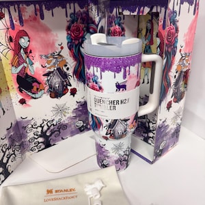May include: A Stanley Quencher H2.0 tumbler featuring a Nightmare Before Christmas theme with purple glitter drip, floral patterns, and character illustrations. The tumbler includes a white handle, a lid, and a branded dust bag with white accessories.