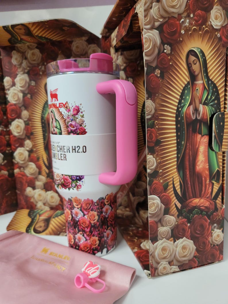 May include: A white Stanley Quencher H2.0 tumbler featuring a pink handle and a floral pattern with an image of the Virgin of Guadalupe. The tumbler is displayed in a decorative box with matching rose imagery and includes a small pink straw topper.