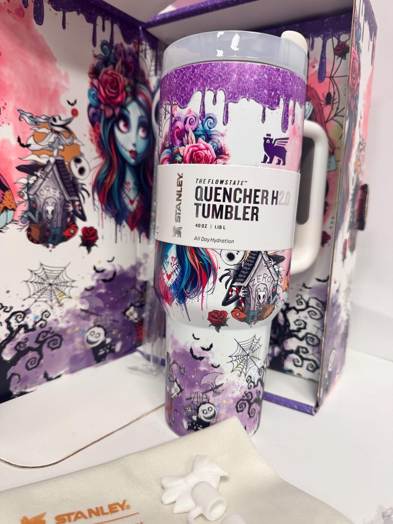 May include: A 40 oz Stanley The Flowstate Quencher H2.0 tumbler featuring a white base with purple glitter drip accents and a graphic print of characters, roses, and spiderwebs. The tumbler includes a white handle, a clear lid, and a white straw.