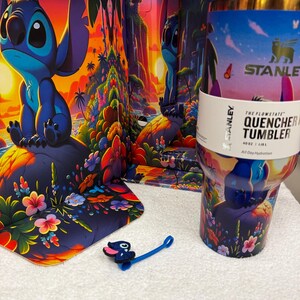Może przedstawiać: Kubek Stanley Flowstate Quencher o pojemności 1,18 litra z kolorową tropikalną sceną przedstawiającą Stitcha, palmy i kwiaty. Kubek zawiera niebieską nakładkę na słomkę w kształcie Stitcha i jest prezentowany na tle pasującego opakowania.