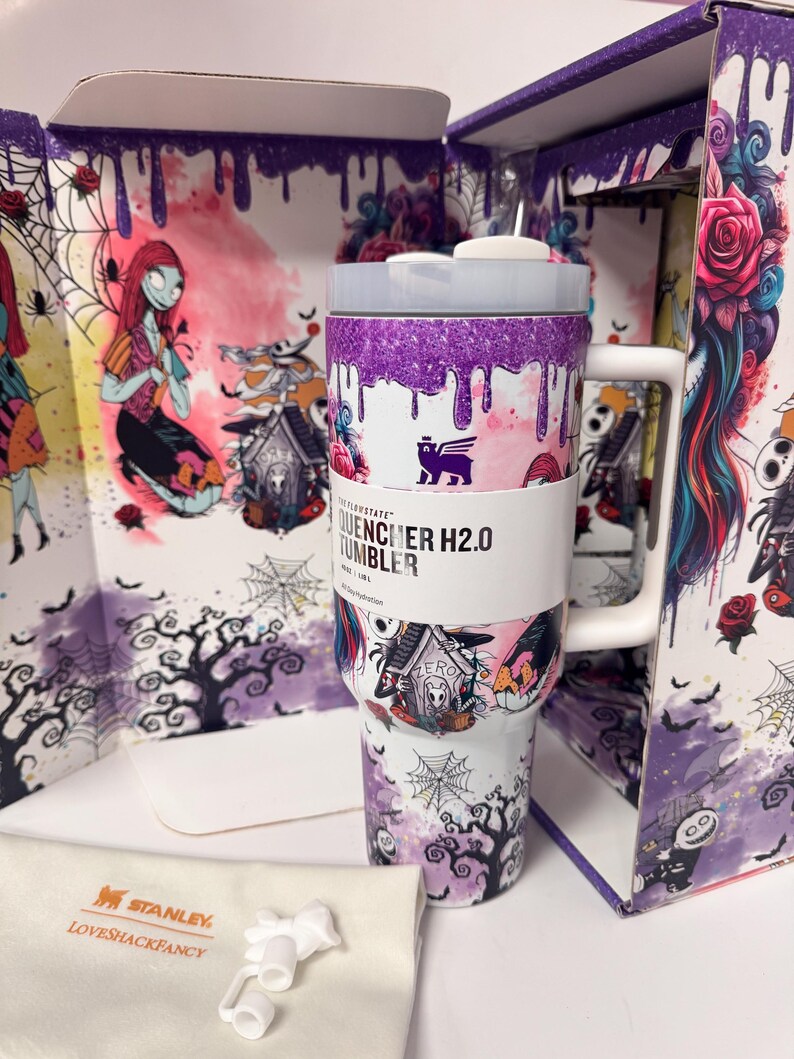 May include: A white Stanley Quencher H2.0 tumbler featuring a purple glitter drip design at the top and a Nightmare Before Christmas graphic print. The tumbler includes a white handle, a lid, and a white dust bag with Stanley LoveShackFancy text.
