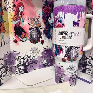 May include: A white Stanley Flowstate Quencher H2.0 tumbler with a 40oz capacity, featuring a purple glitter drip design at the top and a Nightmare Before Christmas graphic print. It includes a white handle, a lid, and a separate white straw attachment.