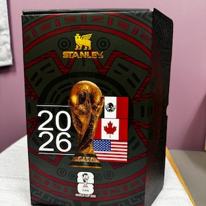 May include: A rectangular Stanley brand product box featuring a black and red graphic design. The box displays the FIFA World Cup 2026 trophy, the text 20 26, the FIFA World Cup 2026 logo, and the national flags of Mexico, Canada, and the United States.